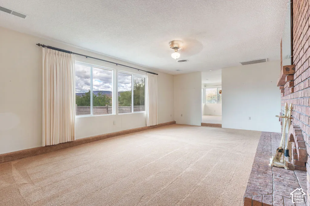 Spacious room with light-colored carpeting, a brick fireplace, and a large window wall