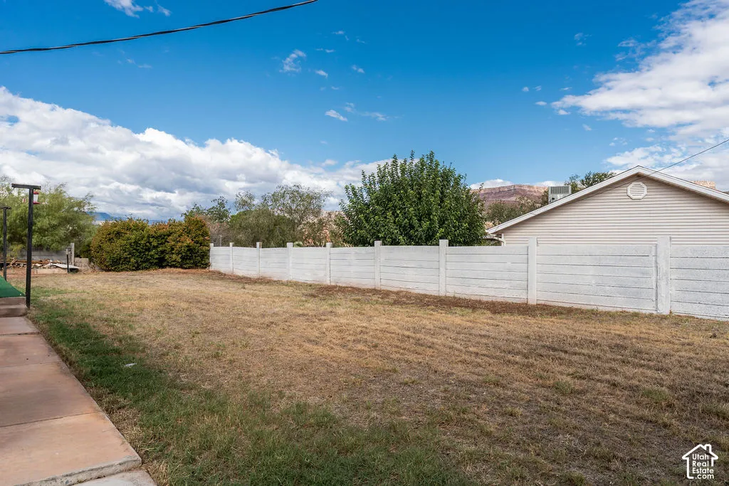 Expansive backyard featuring a concrete patio, mature landscaping, and a white panel fence