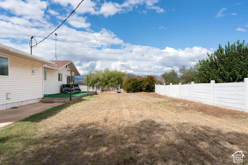 Expansive outdoor space featuring a white privacy fence, mature perimeter landscaping, and a side patio with artificial turf