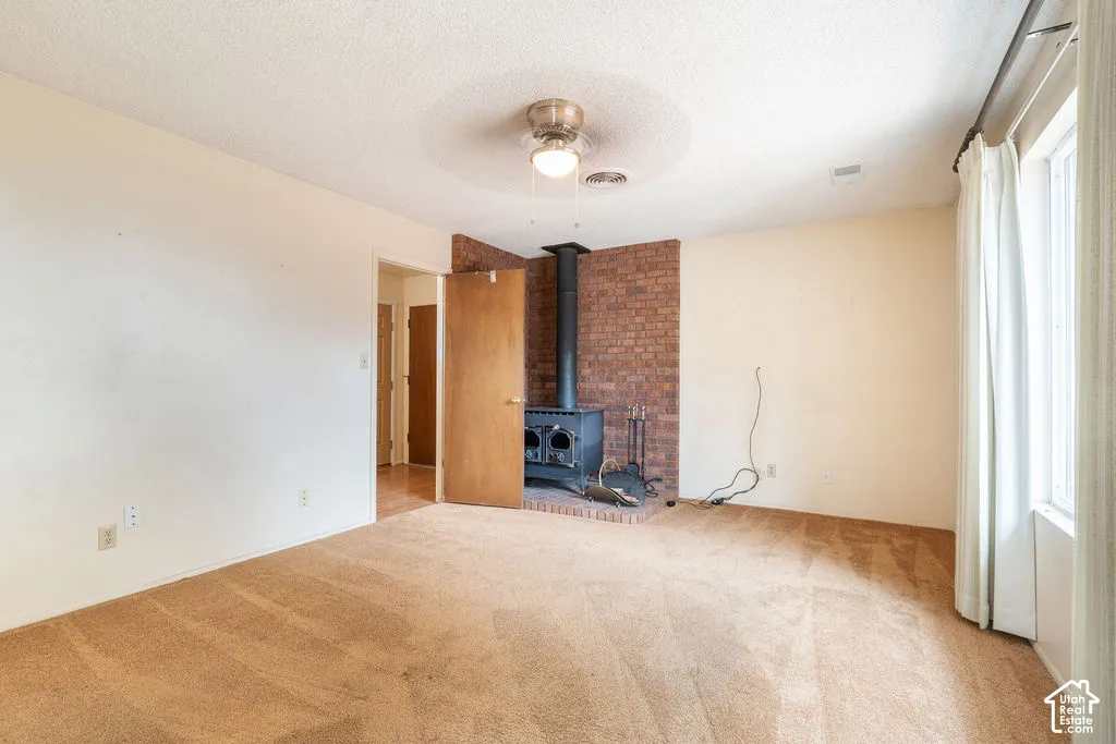 Spacious room featuring a wood-burning stove with a brick surround, a ceiling fan, and window with vertical blinds