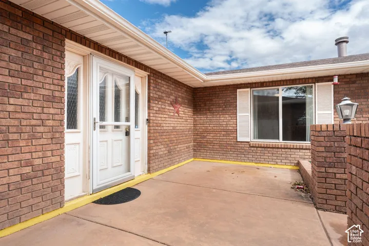 Brick exterior with a covered entry, white storm door, and a large window with white shutters