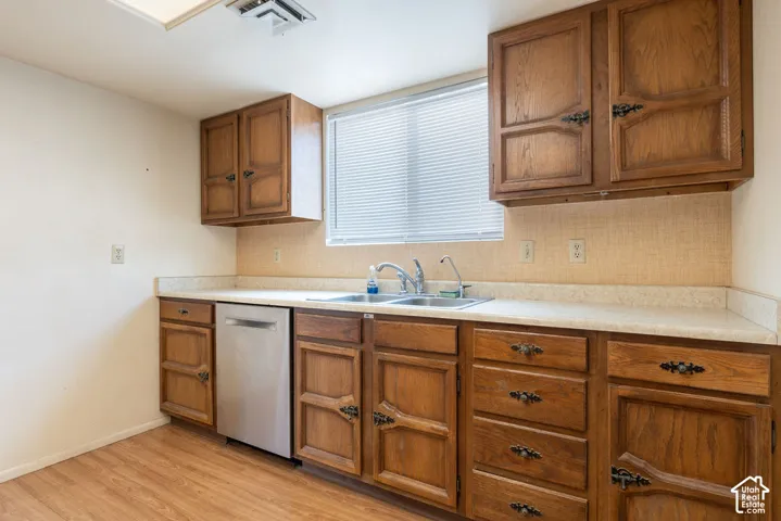 Wood-finish flooring, wood cabinetry with decorative hardware, stainless steel dishwasher, double basin sink, and a window with blinds