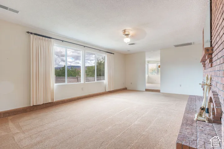 Spacious room with light-colored carpeting, a brick fireplace, and a large window wall