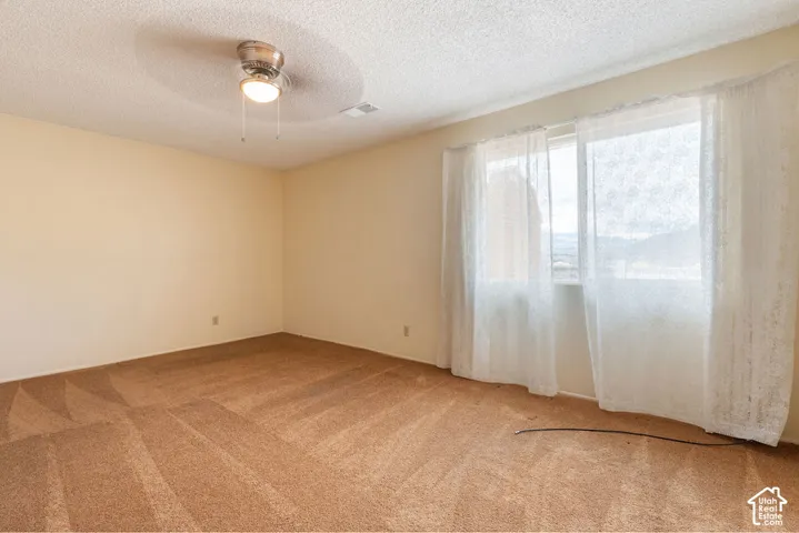 Ceiling fan with integrated lighting, textured ceiling, light-toned walls, two windows, and patterned carpeting