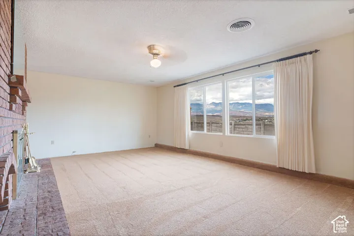 Expansive room featuring a brick fireplace, beige carpeting, and a large window overlooking a mountain landscape