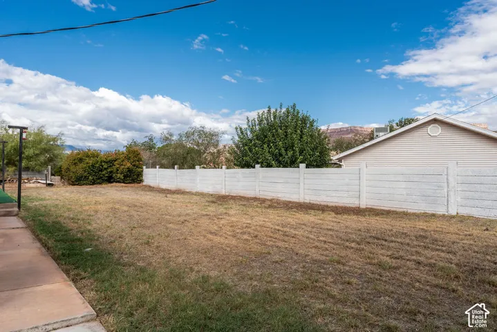 Expansive backyard featuring a concrete patio, mature landscaping, and a white panel fence