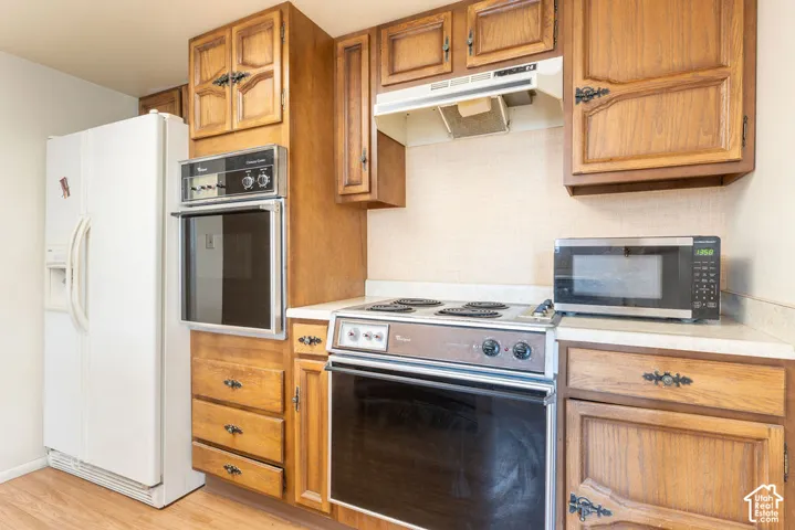 Wood-finish cabinetry, built-in wall oven, built-in cooktop, and light-toned countertops