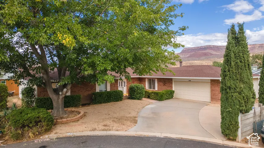 Brick exterior residence with an attached garage, a paved driveway, and mature landscaping