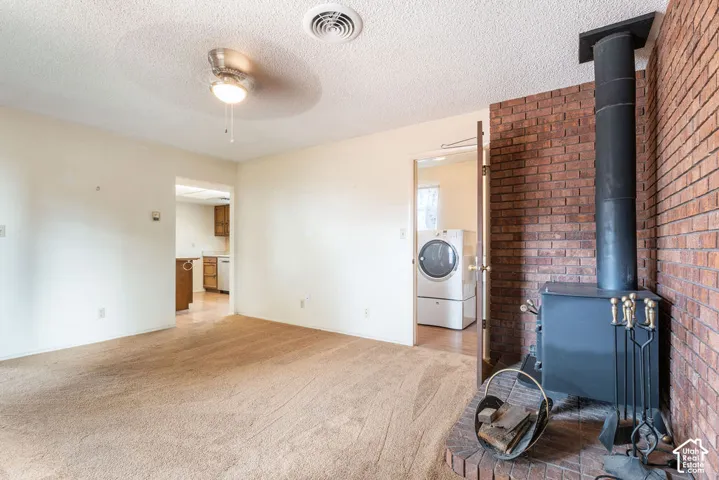 Living area featuring a brick accent wall, wood-burning stove, and ceiling fan