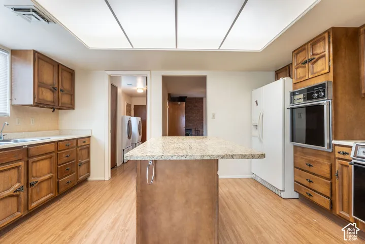 Kitchen featuring wood-finish flooring, wood cabinetry, a built-in oven, and a center island with a light-toned countertop