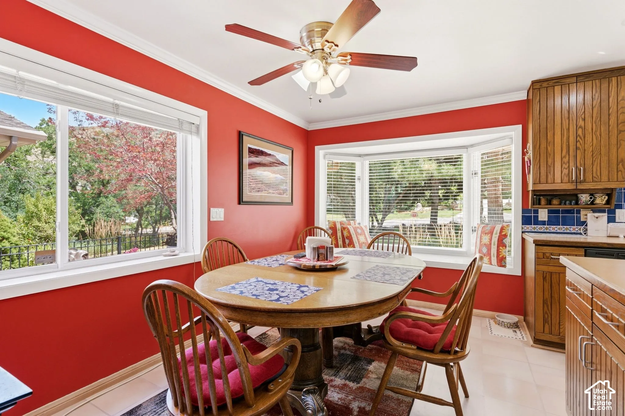 Ceiling fan with light fixture, large windows, bay window, wood cabinetry, and tile flooring