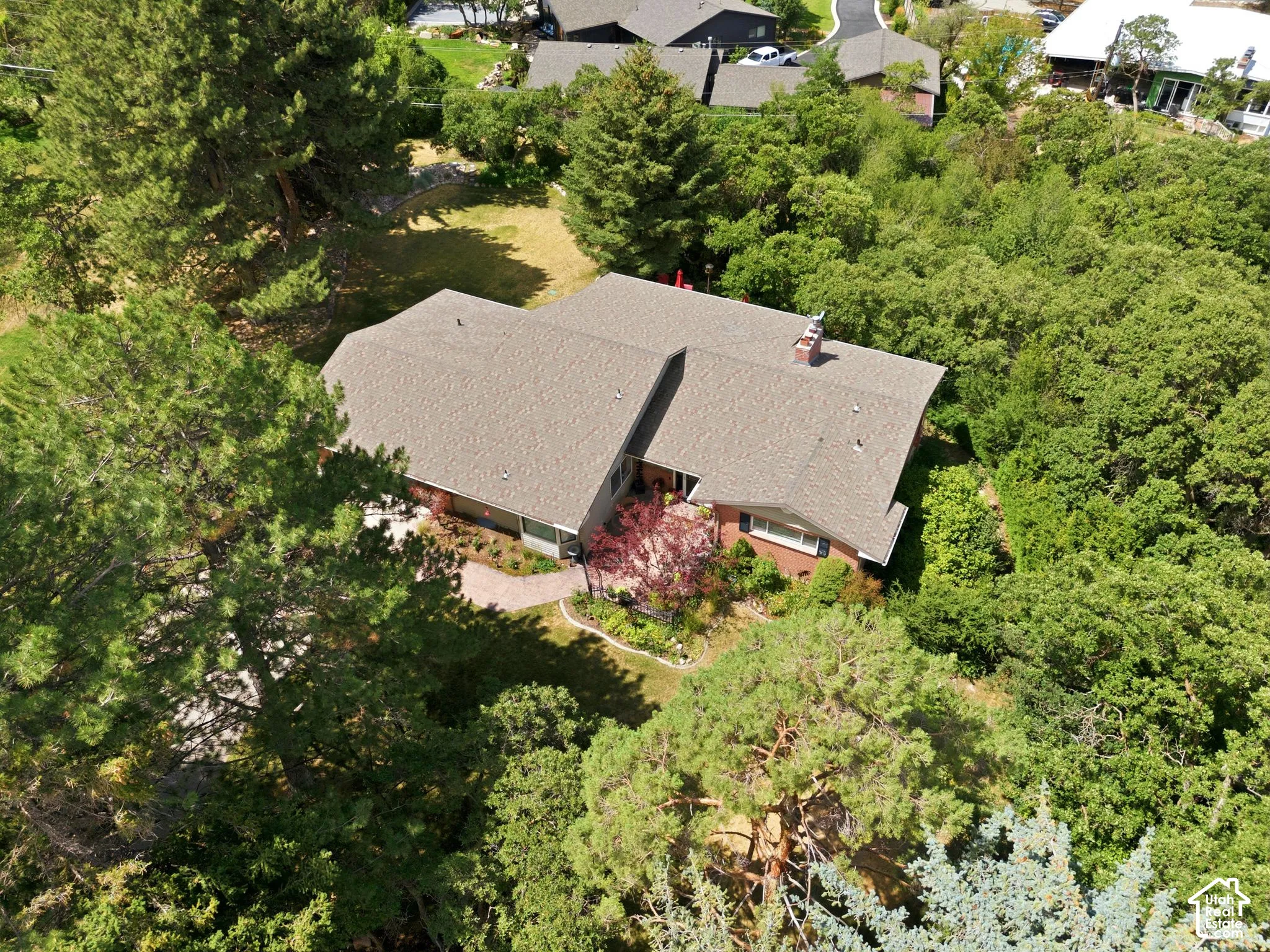 Property featuring a gabled roof, brick exterior, and lush surrounding landscaping