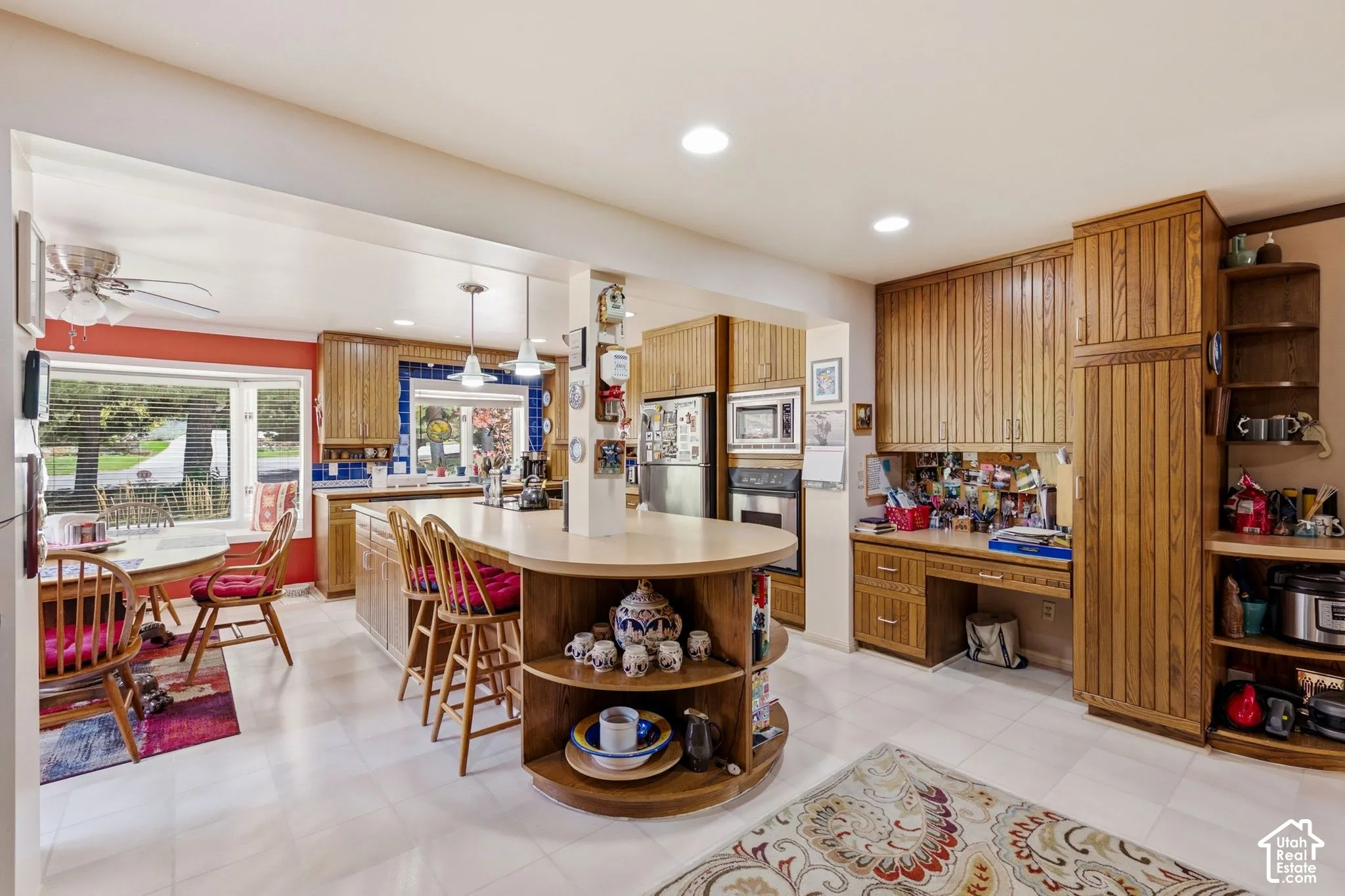 L-shaped kitchen island with integrated shelving, built-in desk area, recessed lighting, and wood-finish cabinetry