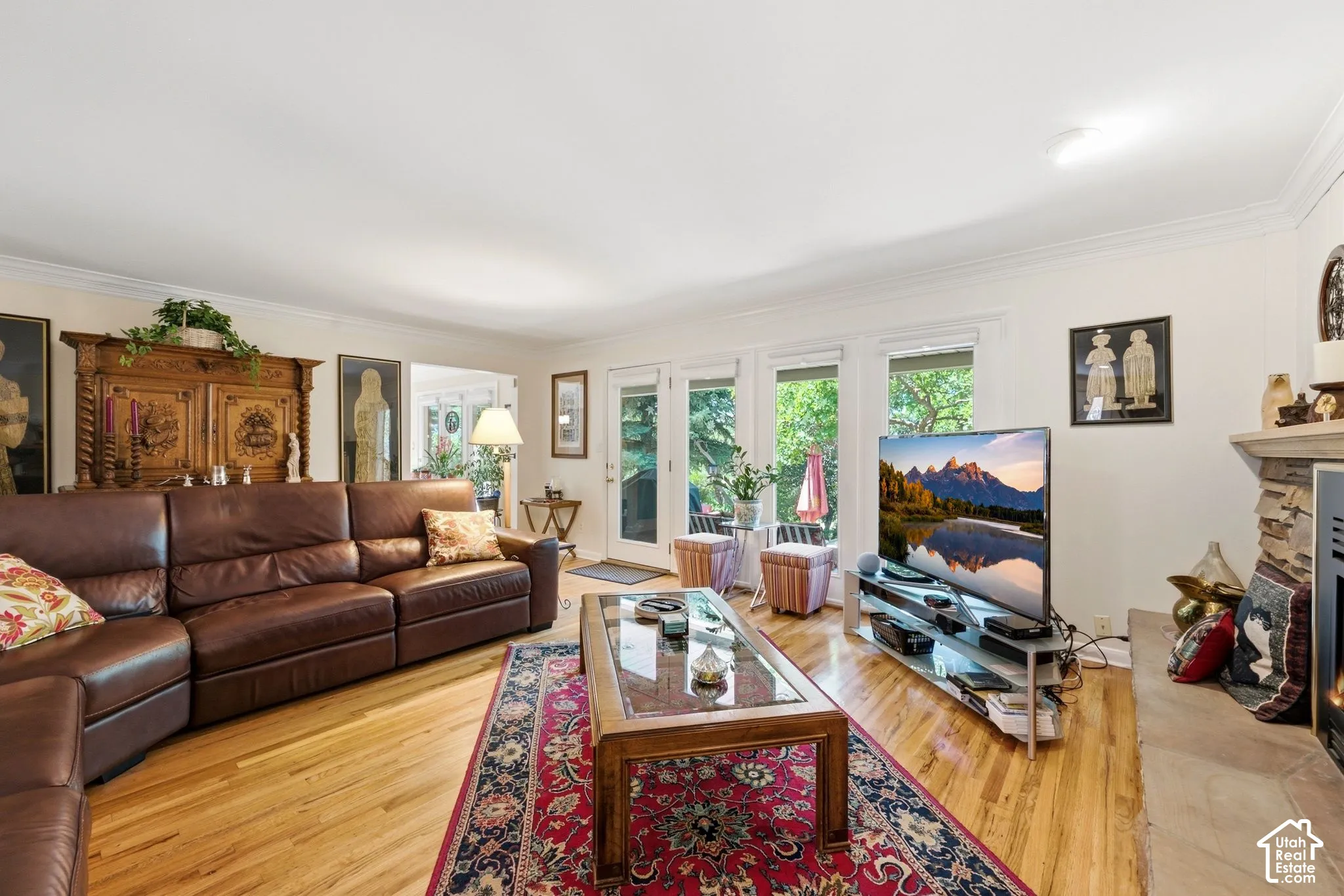 Hardwood flooring, crown molding, stone-clad fireplace, and multiple windows
