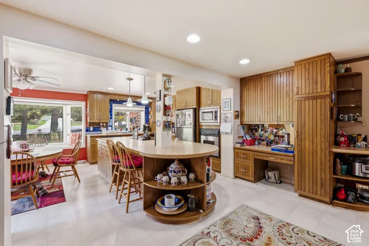 L-shaped kitchen island with integrated shelving, built-in desk area, recessed lighting, and wood-finish cabinetry