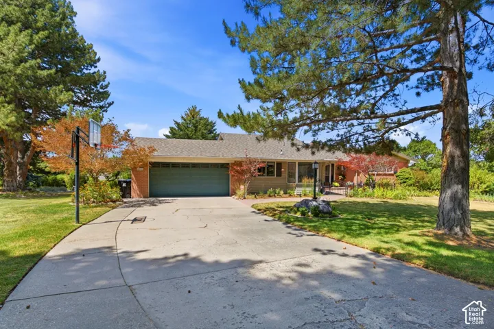 Expansive concrete driveway, mature landscaping, integrated two-car garage, brick exterior, and a covered front entry