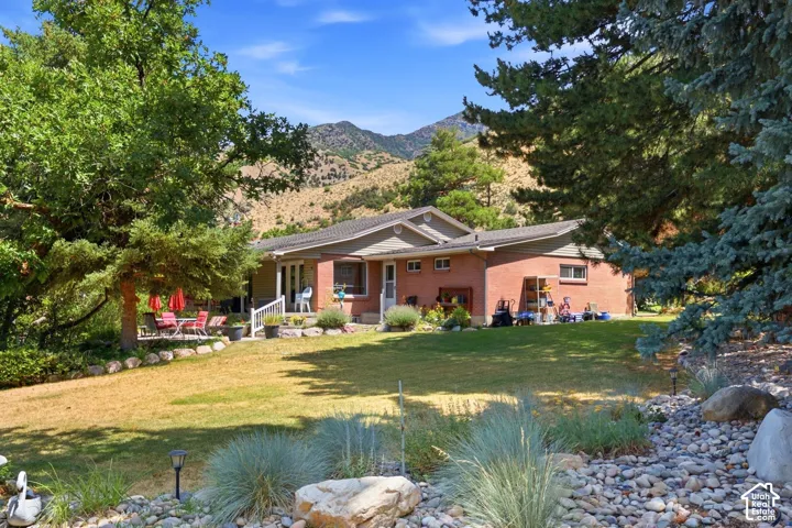 Expansive lawn area with mature trees, a stone patio, and a brick exterior dwelling