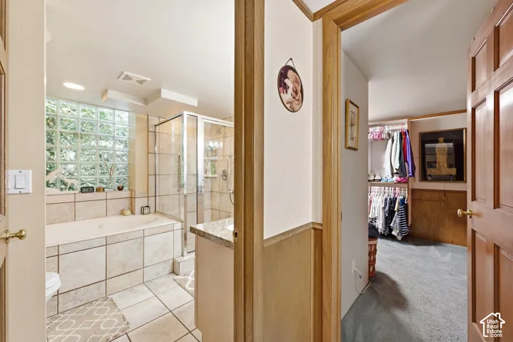 Bathroom featuring a built-in tub, glass block window, tiled shower enclosure, and a vanity with a stone countertop