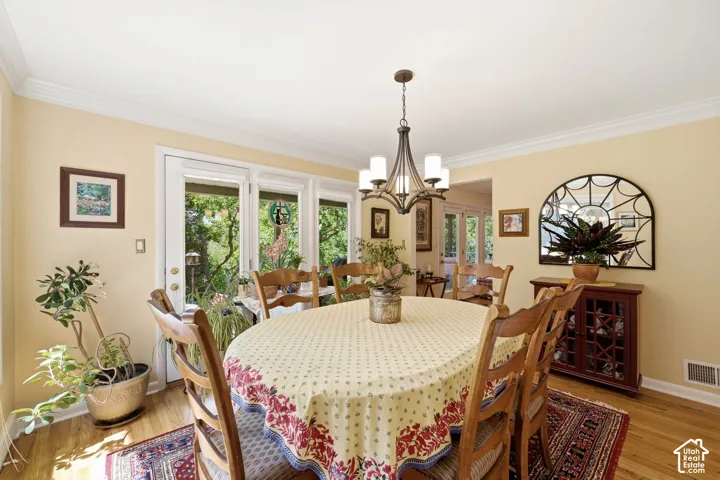 Hardwood flooring, crown molding, white trim, glass-paned door, and a chandelier with white glass shades