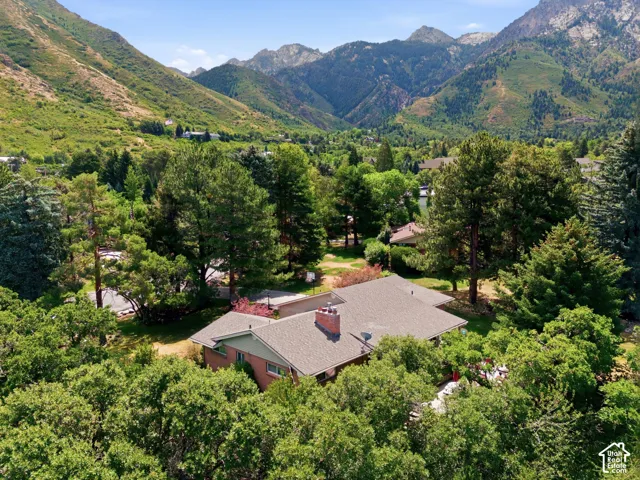 Property surrounded by mature trees, featuring a gabled roofline and a prominent brick chimney, set against a mountainous backdrop