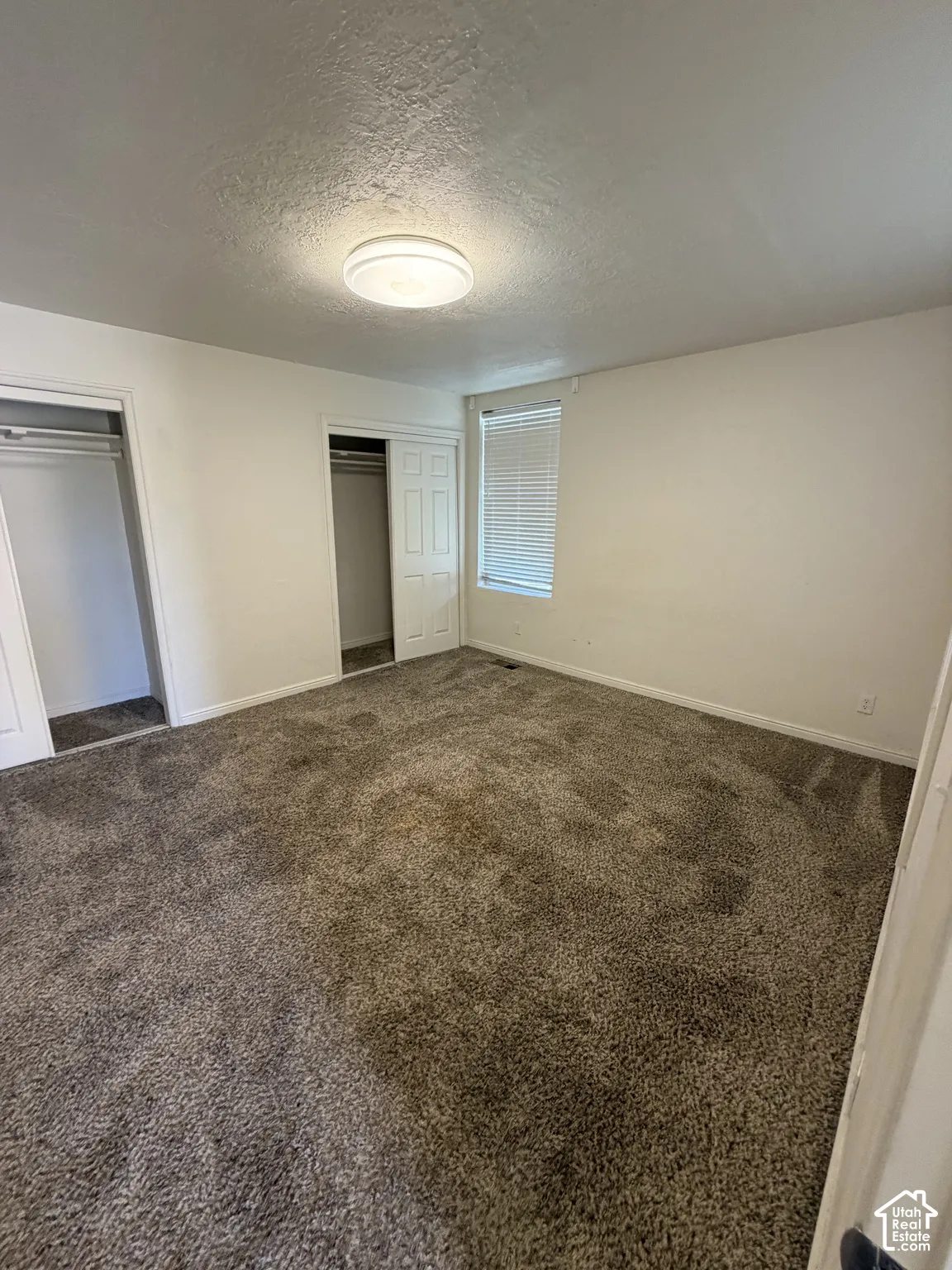 Textured ceiling with a flush-mount light fixture, window with blinds, and wall-to-wall carpeting