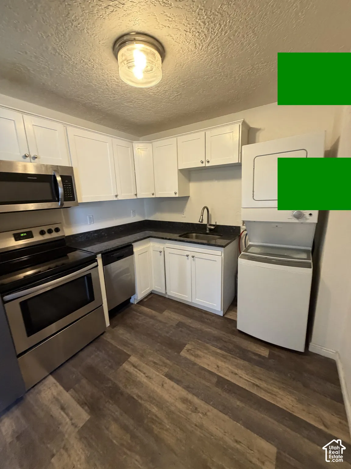 Kitchen featuring stainless steel appliances, white cabinetry, dark countertops, and wood-finish flooring