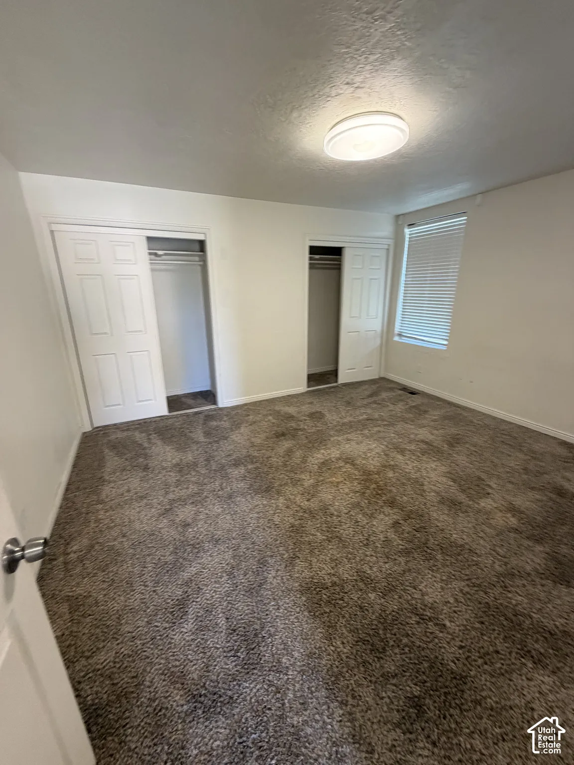 Carpeted room featuring dual sliding door closets, a window with horizontal blinds, and a flush-mount ceiling light fixture