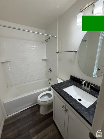 Bathroom featuring a white subway tile shower, white bathtub, dark wood-finish flooring, white vanity with a dark countertop, and an oval mirror