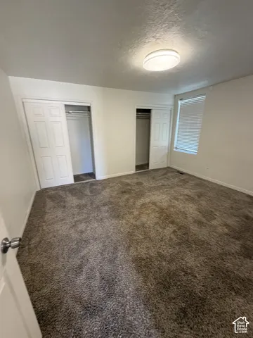 Carpeted room featuring dual sliding door closets, a window with horizontal blinds, and a flush-mount ceiling light fixture