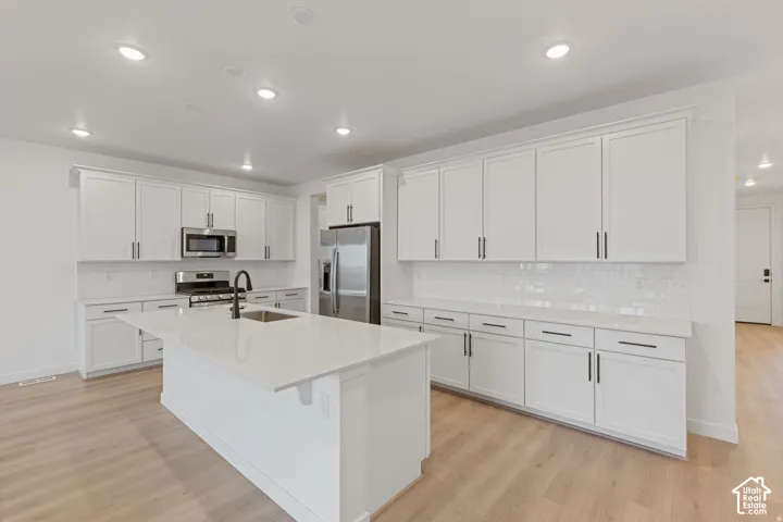Kitchen featuring white shaker-style cabinetry, a central island with a sink, stainless steel appliances, and wood-finish flooring