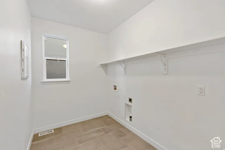 Neutral tone wall paint, tile flooring, window with white trim, wall-mounted shelving, and utility hookups