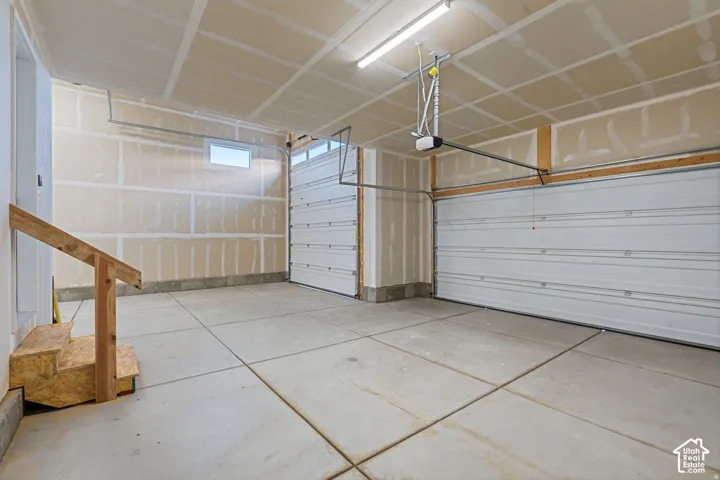 Concrete flooring, overhead lighting, two garage doors, built-in stairs, and a small window