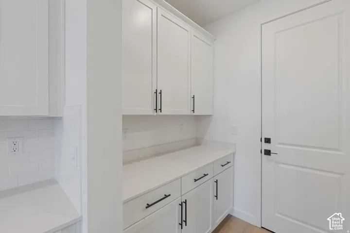 White shaker cabinetry with matte black hardware, light-toned countertop, white subway tile backsplash, and light wood-finish flooring