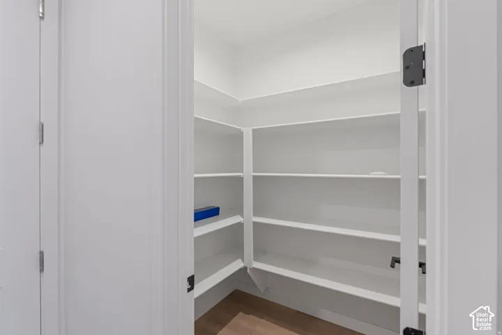 Walk-in pantry with multiple white shelves and wood-finish flooring
