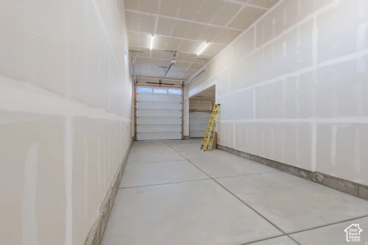 Unfinished drywall interior, concrete flooring, overhead lighting, and two overhead garage doors