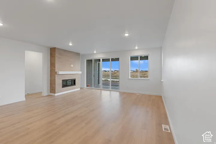 Tile-clad fireplace with a built-in firebox, recessed lighting, wood-finish flooring, white walls, and a sliding glass door to the exterior