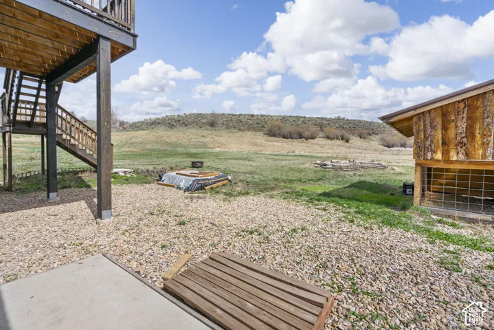 Expansive gravel yard with concrete patio, wood deck, wood staircase, and wood-sided outbuilding