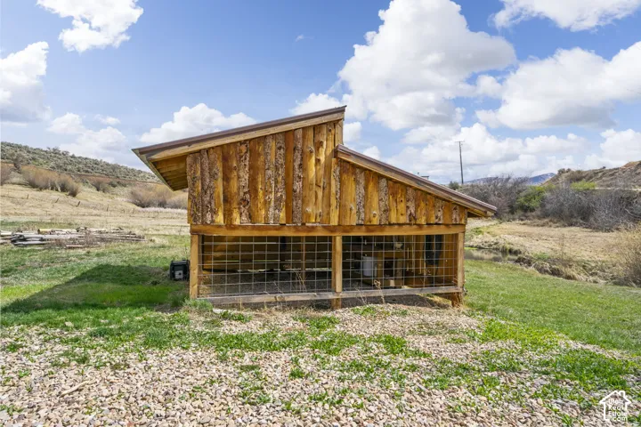 Wood-sided outbuilding with a sloped roof, featuring a metal gutter system and wire mesh enclosure