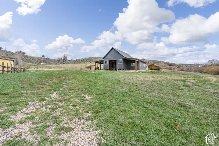 Expansive green space with distant rolling hills and a modern barn-style structure featuring a covered porch