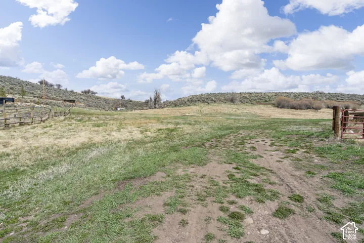 Expansive open land featuring natural grass, a partial wood fence, and a red metal gate