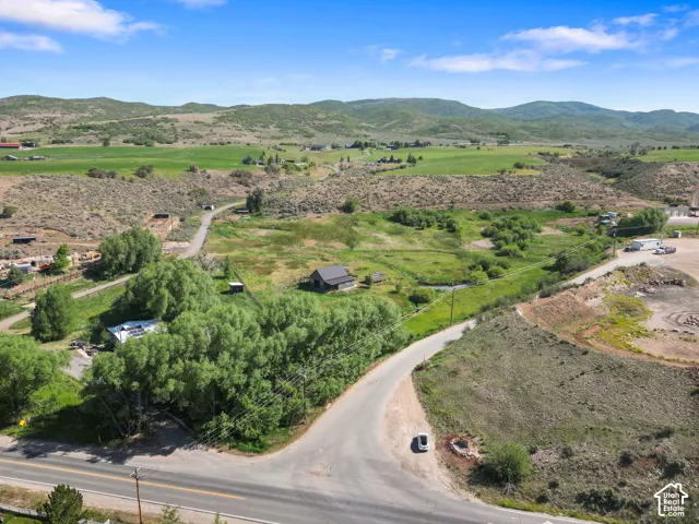 Expansive rural property featuring a winding road, lush green fields, and distant mountainous terrain