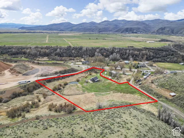 Expansive land parcel featuring a residential structure, surrounding green space, and distant mountain backdrops