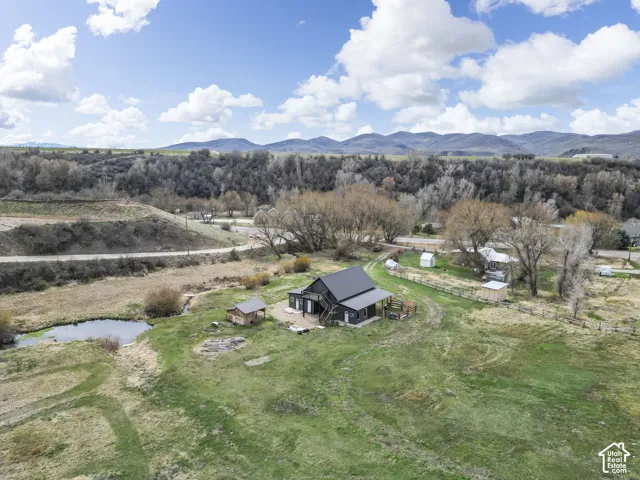 Expansive property featuring a dark-clad exterior, a black roof, a pond, and surrounding mountainous terrain