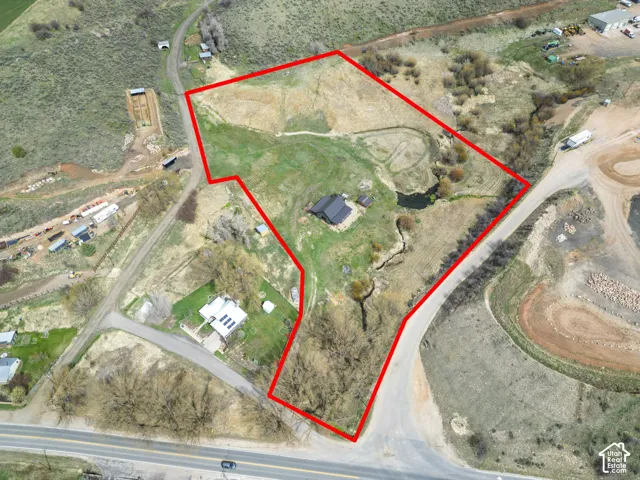 Expansive property featuring a dark-roofed residence, a natural pond, and cultivated land, bordered by a paved road