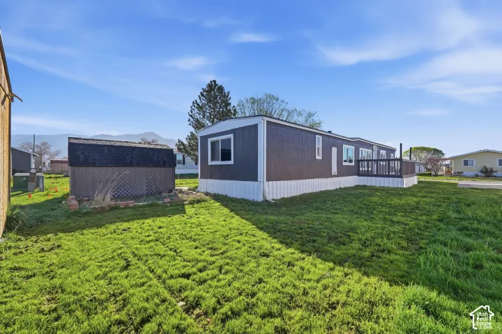 Expansive grassy yard with a built-in storage shed featuring a shingled roof, a dark-colored exterior, and an exterior deck with railing