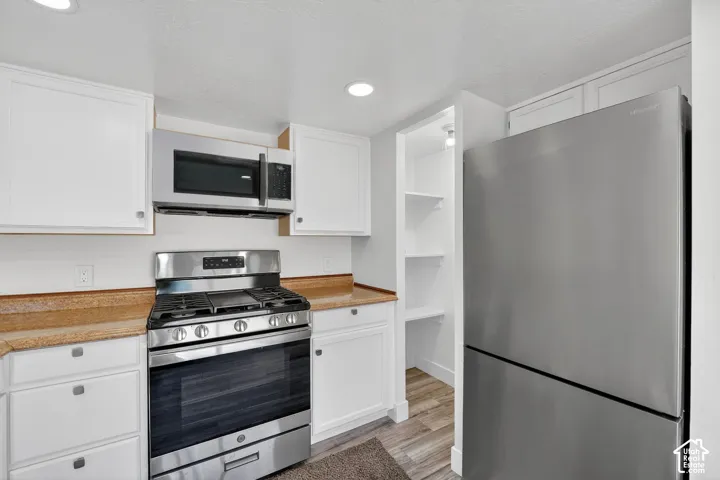 White cabinetry with contrasting countertops, stainless steel appliances, and built-in shelving
