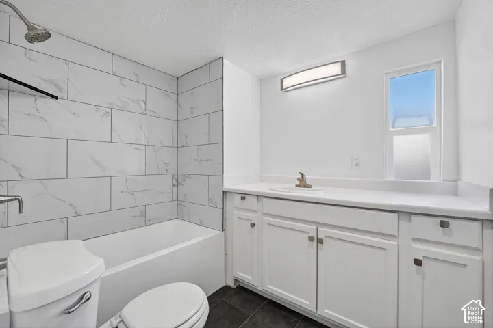 White subway tile shower surround, built-in bathtub, white vanity with integrated sink, white countertop, and dark-finish flooring