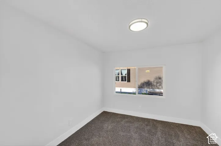 White interior walls with a single window, overhead flush-mount light fixture, and dark carpet flooring