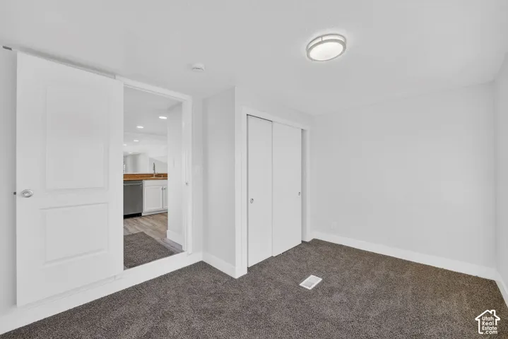 White interior walls, modern flush mount ceiling light, dark gray carpeted flooring, white bi-fold closet doors, and a white interior door with a silver knob