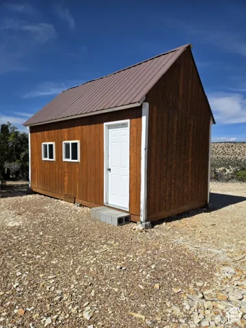 Wood-sided structure with a brown metal roof, white paneled door, and two white-framed windows